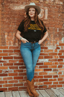 Female model wearing our Waltz With Me shirt. Black t-shirt with orange letters that say Waltz With Me. Small Next Waltz logo in white below.