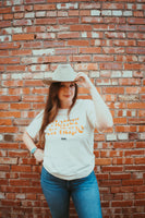 Female model wearing a cowboy hat and wearing our Better On Tape t-shirt. Cream colored short sleeve shirt with the words Better On Tape in orange letter. Small New Waltz logo below in black lettering.